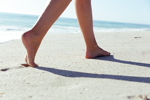 Low section of a Caucasian woman enjoying time at the beach on a sunny day, walking along the beach, with sea in the background