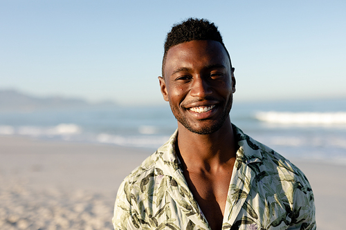 A portrait of a happy, attractive African American man enjoying free time on beach on a sunny day, wearing a Hawaiian shirt, sun shining on his face,. Relaxing summer vacation.