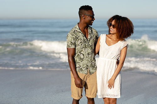 A mixed race couple enjoying free time on beach on a sunny day together, looking at each other and holding each other with sun shining on their faces. Relaxing summer vacation.