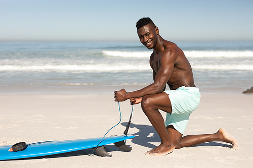 A portrait of a happy, attractive African American man enjoying free time on beach on a sunny day, smiling, having fun, surfing, sun shining on his face.