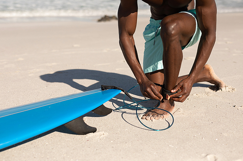 An attractive African American man enjoying free time on beach on a sunny day, having fun, surfing, sun shining on him.