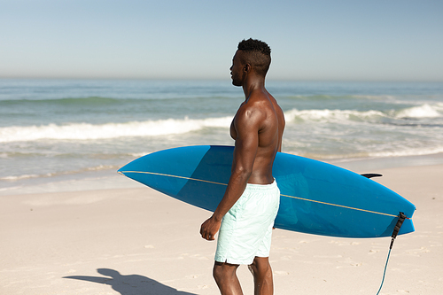 A happy, attractive African American man enjoying free time on beach on a sunny day, having fun, surfing, holding a surfboard, sun shining on his face.