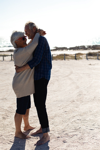 Side view of a senior Caucasian couple sitting at the beach in the sun, embracing and smiling. Weekend beach vacation, lifestyle and leisure.