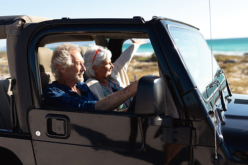 Side view of a senior Caucasian couple sitting in their car, driving to the beach in the sun, the man at the wheel and both smiling