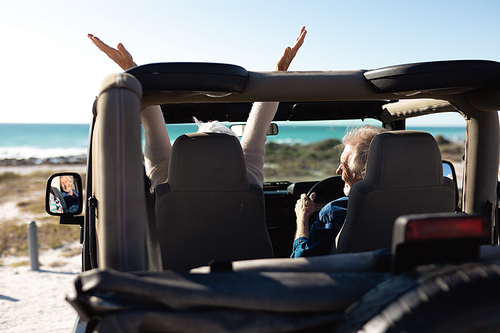 Rear view of a senior Caucasian couple sitting in their car, arriving at the beach in the sun, the man at the wheel and the woman with her arms in the air