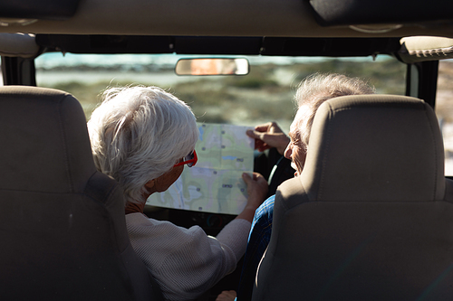 Rear view of a senior Caucasian couple sitting in their car, looking at a road map together, the man at the wheel