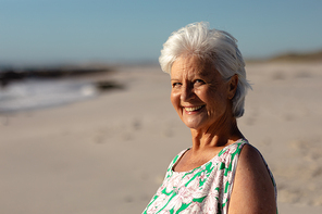 Portrait of a senior Caucasian woman at the beach in the sun, looking to camera and smiling, with blue sky in the background