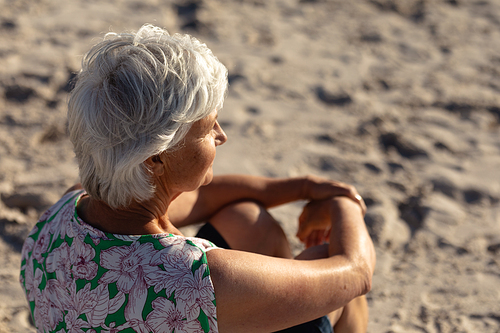 Side view close up of a senior Caucasian woman at the beach in the sun, sitting on the sand and looking out to sea