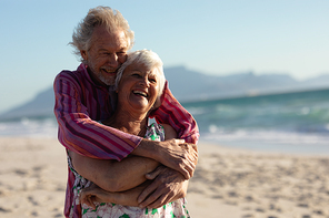 Front view of a senior Caucasian couple at the beach in the sun, embracing and laughing, with blue sky in the background