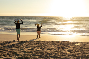 Rear view of a senior Caucasian couple at the beach at sunset, holding surfboards on their heads and walking towards the sea