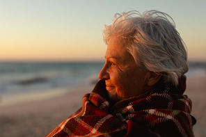 Side view close up of a senior Cacuasian woman standing on the beach at sunset smiling and looking out to sea