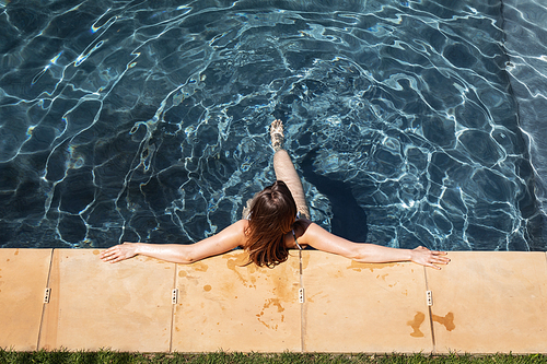 Caucasian woman spending time by swimming pool self isolating, relaxing in water in a swimming pool. Social distancing in quarantine lockdown during coronavirus covid 19 epidemic.