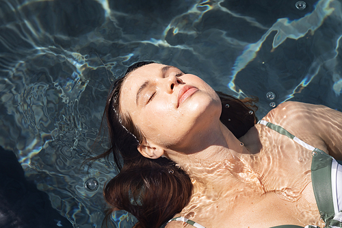 Caucasian woman spending time by swimming pool self isolating, relaxing in water in a swimming pool. Social distancing in quarantine lockdown during coronavirus covid 19 epidemic.