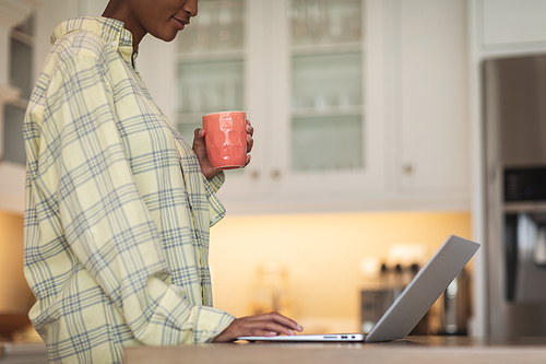 Mixed race woman spending time at home, sitting in her kitchen and using her laptop. Self isolating and social distancing in quarantine lockdown during coronavirus covid 19 epidemic.