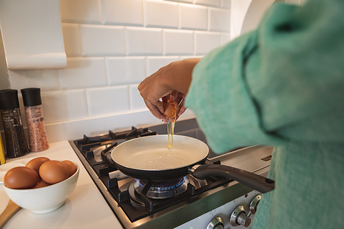 Mid section of a mixed race woman spending time at home in her kitchen, preparing a breakfast. Self isolating and social distancing in quarantine lockdown during coronavirus covid 19 epidemic.