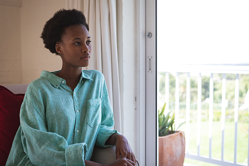 Mixed race woman spending time at home, sitting in her bedroom and looking out the window. Self isolating and social distancing in quarantine lockdown during coronavirus covid 19 epidemic.