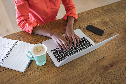 Mid section of a mixed race woman spending time at home, sitting in her kitchen and using her laptop. Self isolating and social distancing in quarantine lockdown during coronavirus covid 19 epidemic.