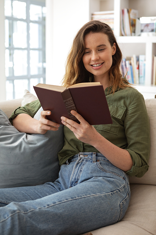 Caucasian woman spending time at home, sitting on sofa, reading a book. Lifestyle at home isolating, social distancing in quarantine lockdown during coronavirus covid 19 pandemic.