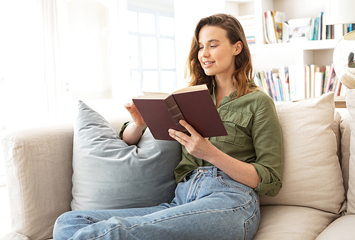 Caucasian woman spending time at home, sitting on sofa, reading a book. Lifestyle at home isolating, social distancing in quarantine lockdown during coronavirus covid 19 pandemic.