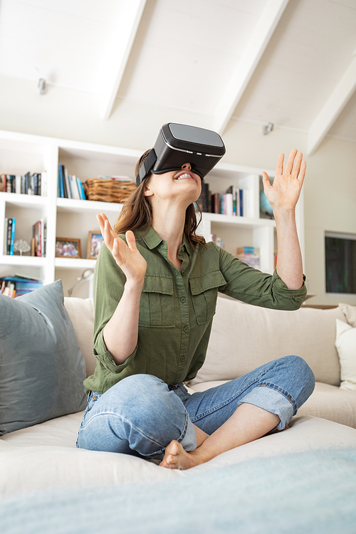A Caucasian woman spending time at home, sitting on sofa, using VR headset. Lifestyle at home isolating, social distancing in quarantine lockdown during coronavirus covid 19 pandemic.