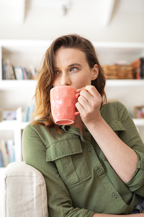 Caucasian woman spending time at home, sitting on sofa, drinking coffee from a mug. Lifestyle at home isolating, social distancing in quarantine lockdown during coronavirus covid 19 pandemic.