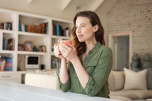 Caucasian woman spending time at home, sitting on chair, drinking coffee from a mug. Lifestyle at home isolating, social distancing in quarantine lockdown during coronavirus covid 19 pandemic.