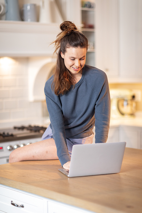 Caucasian woman spending time at home, sitting in the kitchen, using her laptop. Lifestyle at home isolating, social distancing in quarantine lockdown during coronavirus covid 19 pandemic.