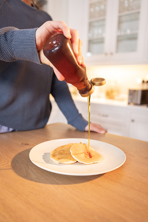 Caucasian woman spending time at home in the kitchen pouring syrup on her pancakes. Lifestyle at home isolating, social distancing in quarantine lockdown during coronavirus covid 19 pandemic.