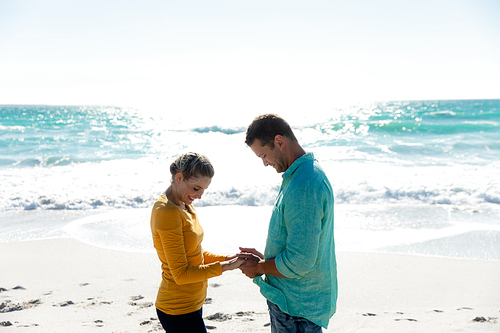 Front view of a Caucasian couple standing on the beach with blue sky and sea in the background, holding hands and smiling