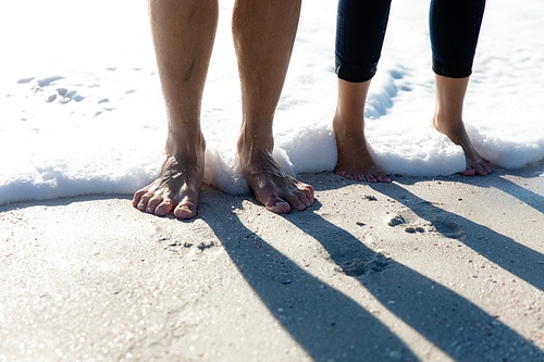 Low section close up of a Caucasian couple standing in the water with their feet covered in foam. Weekend beach vacation, lifestyle and leisure.