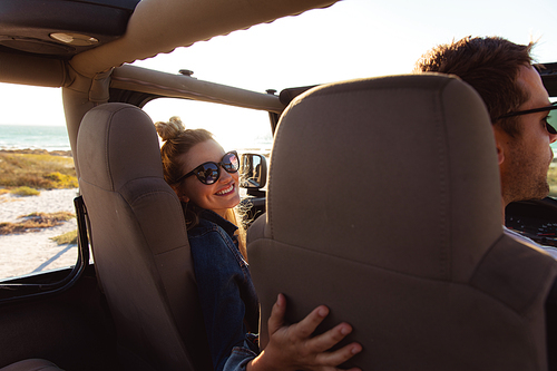 Rear view of a Caucasian couple sitting inside an open top car, the man driving and the woman smiling to camera