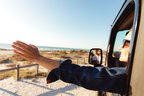 Side view of a Caucasian woman inside an open top car, waving her hand from the window. Weekend beach vacation, lifestyle and leisure.