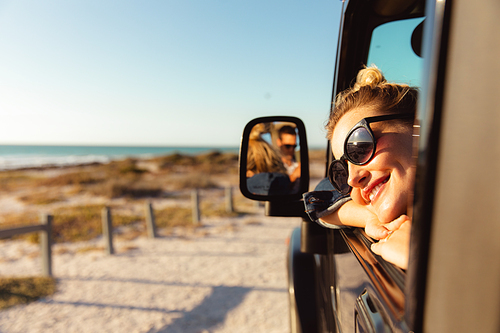 Side view of a Caucasian woman inside an open top car, looking through the window and smiling. Weekend beach vacation, lifestyle and leisure.