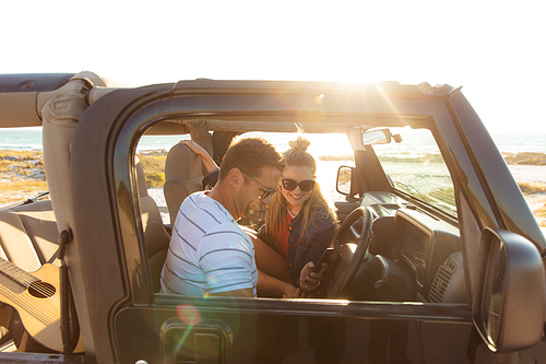 Side view of a Caucasian couple inside an open top car, smiling during a sunset. Weekend beach vacation, lifestyle and leisure.