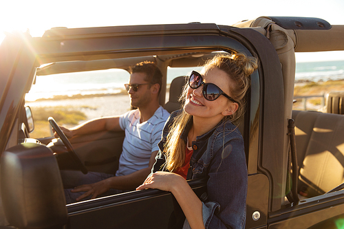 Side view of a Caucasian couple inside an open top car, the man driving, the woman looking through the window and smiling