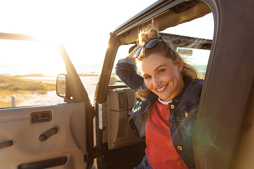 Front view close up of a Caucasian woman inside an open top car with its door open, smiling to camera