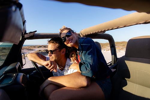 Front view of a Caucasian couple inside an open top car, embracing and smiling. Weekend beach vacation, lifestyle and leisure.