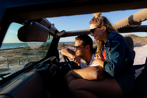 Side view of a Caucasian couple inside an open top car, embracing and looking away. Weekend beach vacation, lifestyle and leisure.
