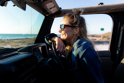Side view of a Caucasian woman inside an open top car, holding a steering wheel, smiling and looking away. Weekend beach vacation, lifestyle and leisure.