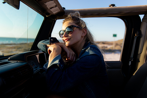 Front view of a Caucasian woman inside an open top car, holding a steering wheel and looking away. Weekend beach vacation, lifestyle and leisure.
