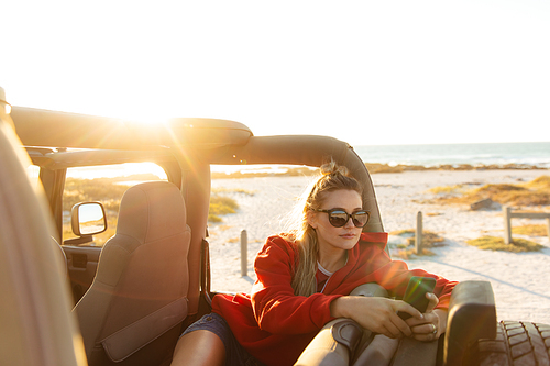 Front view of a Caucasian woman inside an open top car, looking away during the sunset. Weekend beach vacation, lifestyle and leisure.