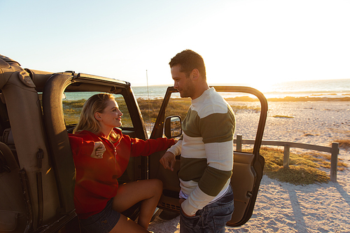 Side view of a Caucasian couple inside an open top car with its door open, looking at each other and smiling