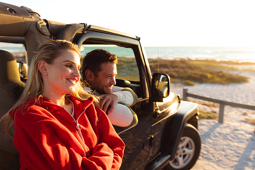 Side view of a Caucasian couple, the man inside an open top car, the woman outside it, smiling and looking away