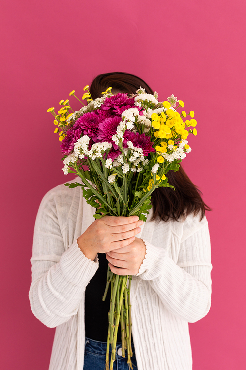 Caucasian woman covering her face with bouquet of flowers on pink. nature summer colour flower beauty.