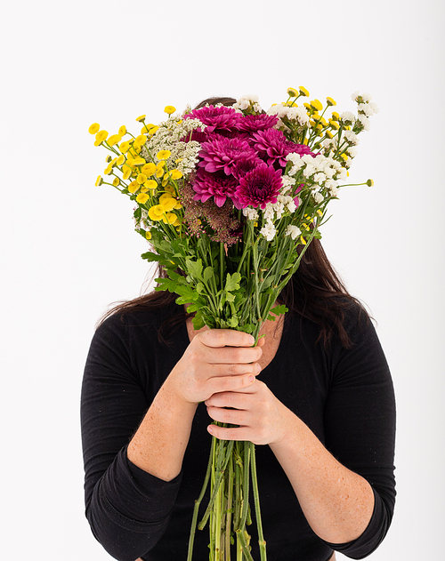 Caucasian woman covering her face with bouquet of flowers on white. nature summer colour flower beauty.