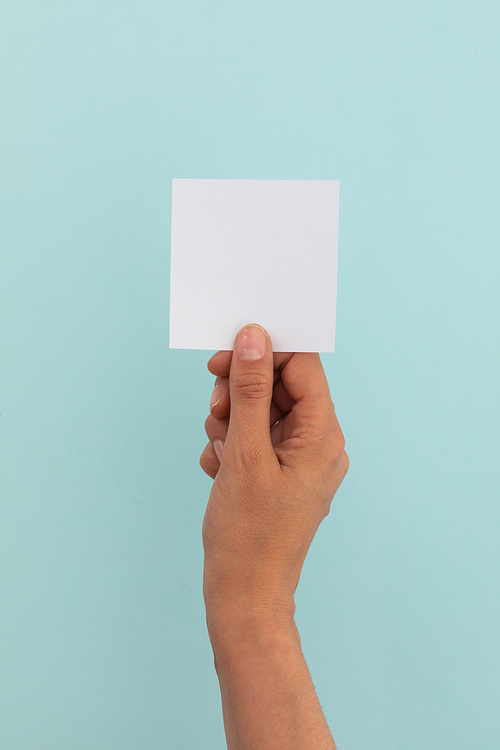 Hand of caucasian woman holding white paper over pale blue background. greetings message copy space.