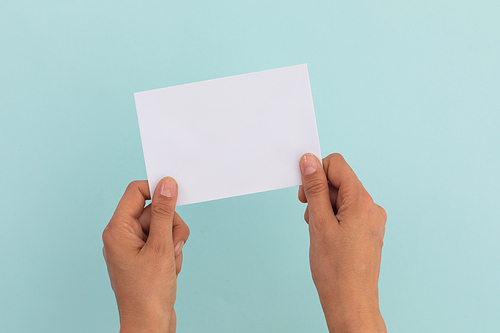 Two hands of caucasian woman holding white paper over pale blue background. greetings message copy space.