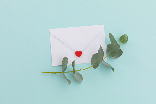 White envelope with heart and twig and leaves lying on pale blue background. love romance valentine's day greetings message letter copy space.