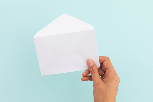 Hand of caucasian woman holding white opened envelope over pale blue background. greetings message copy space.