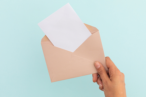 Hand of caucasian woman holding opened envelope with letter over pale blue background. greetings message copy space.